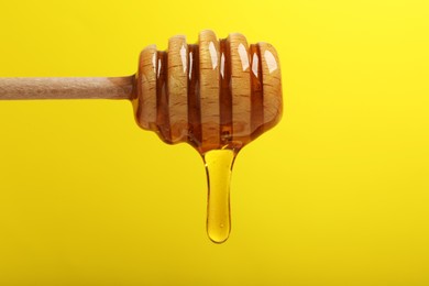 Photo of Delicious honey flowing down from dipper against yellow background, closeup