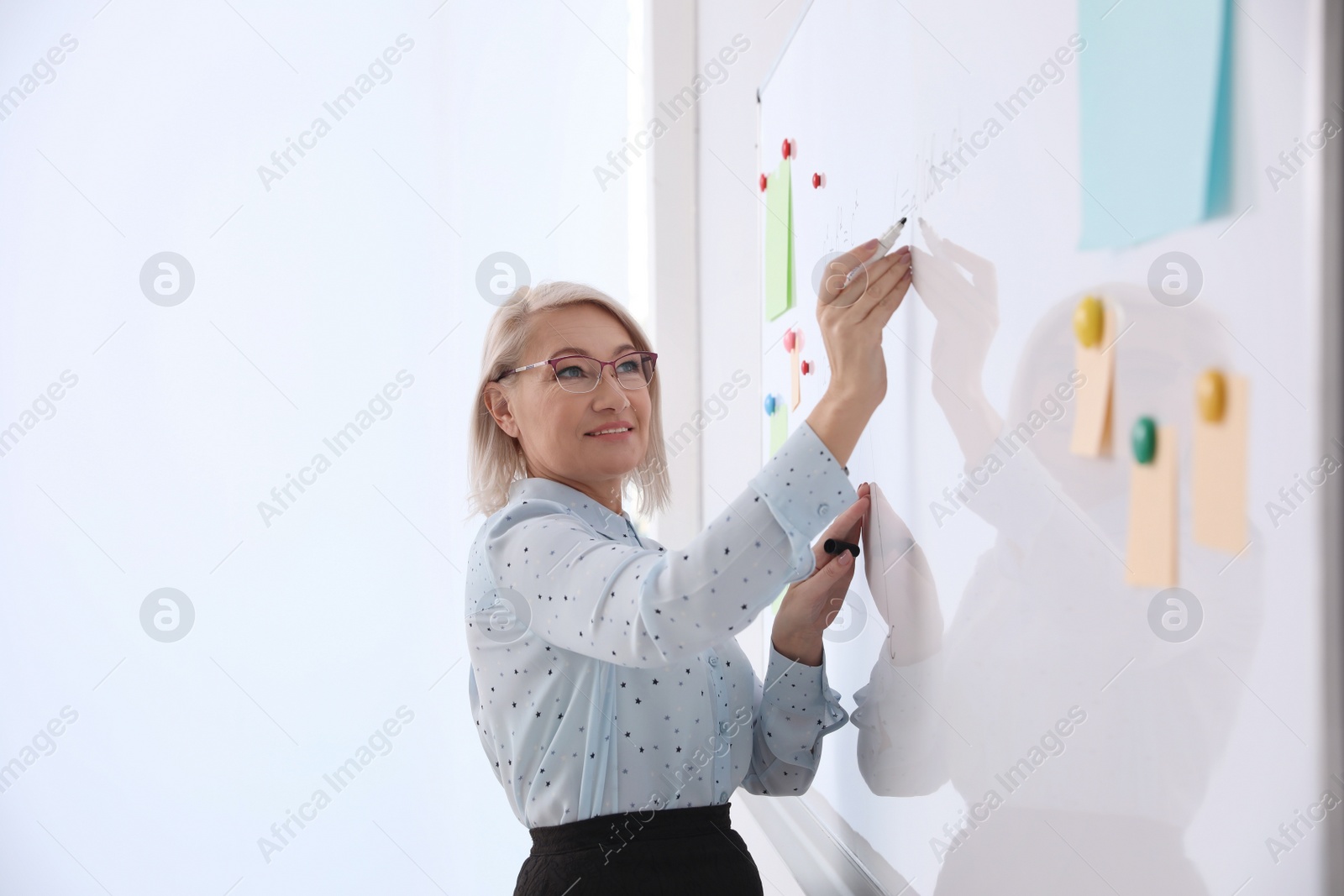 Photo of Mature teacher writing on whiteboard in modern classroom