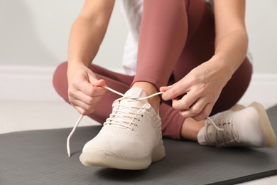 Photo of Woman tying sport shoe lace on floor indoors, closeup