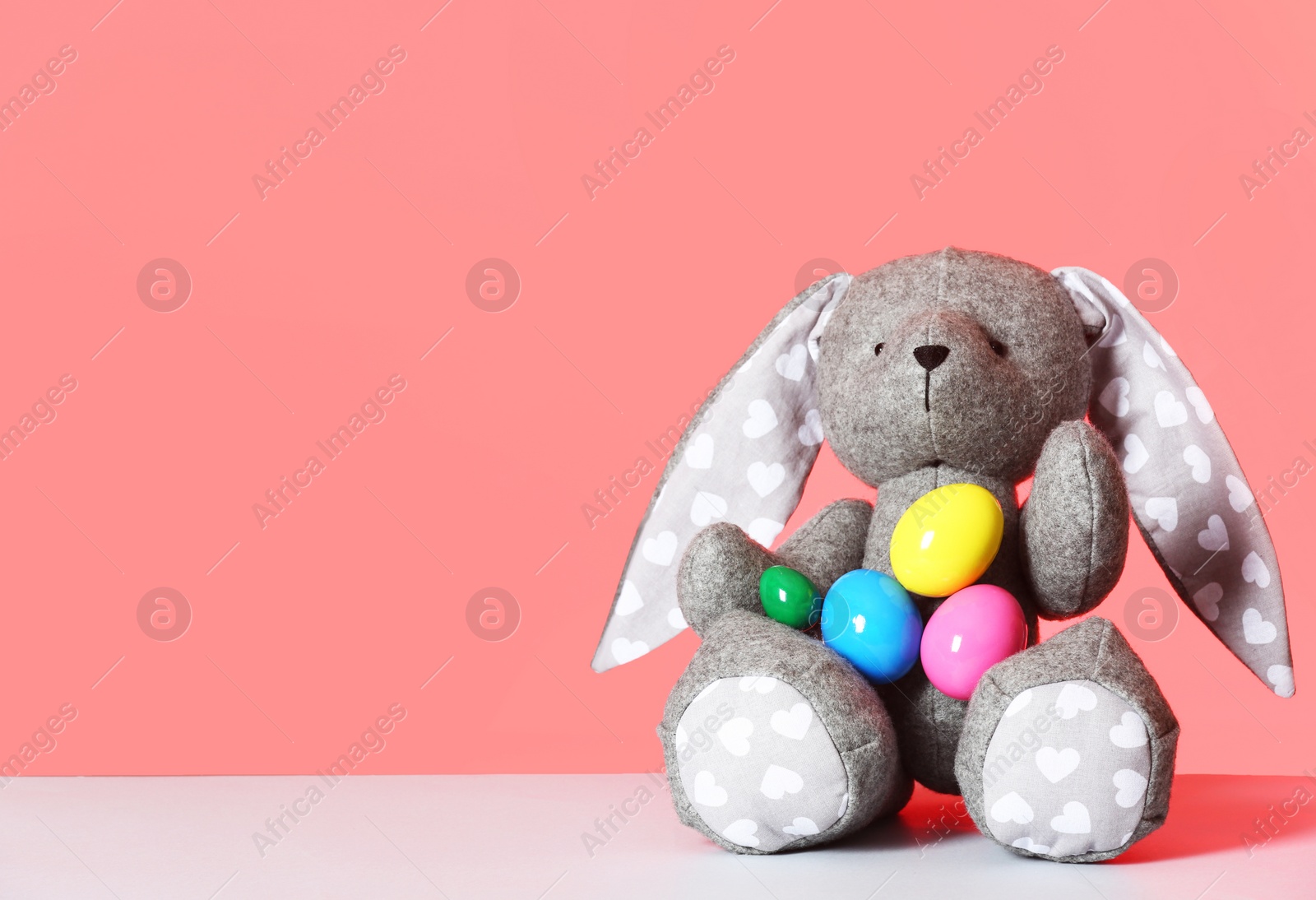 Photo of Cute toy Easter bunny and eggs on table against color background, space for text