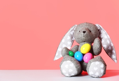 Cute toy Easter bunny and eggs on table against color background, space for text