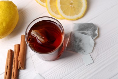 Photo of Tea bags, glass of hot drink, cinnamon sticks and lemons on white wooden table, above view