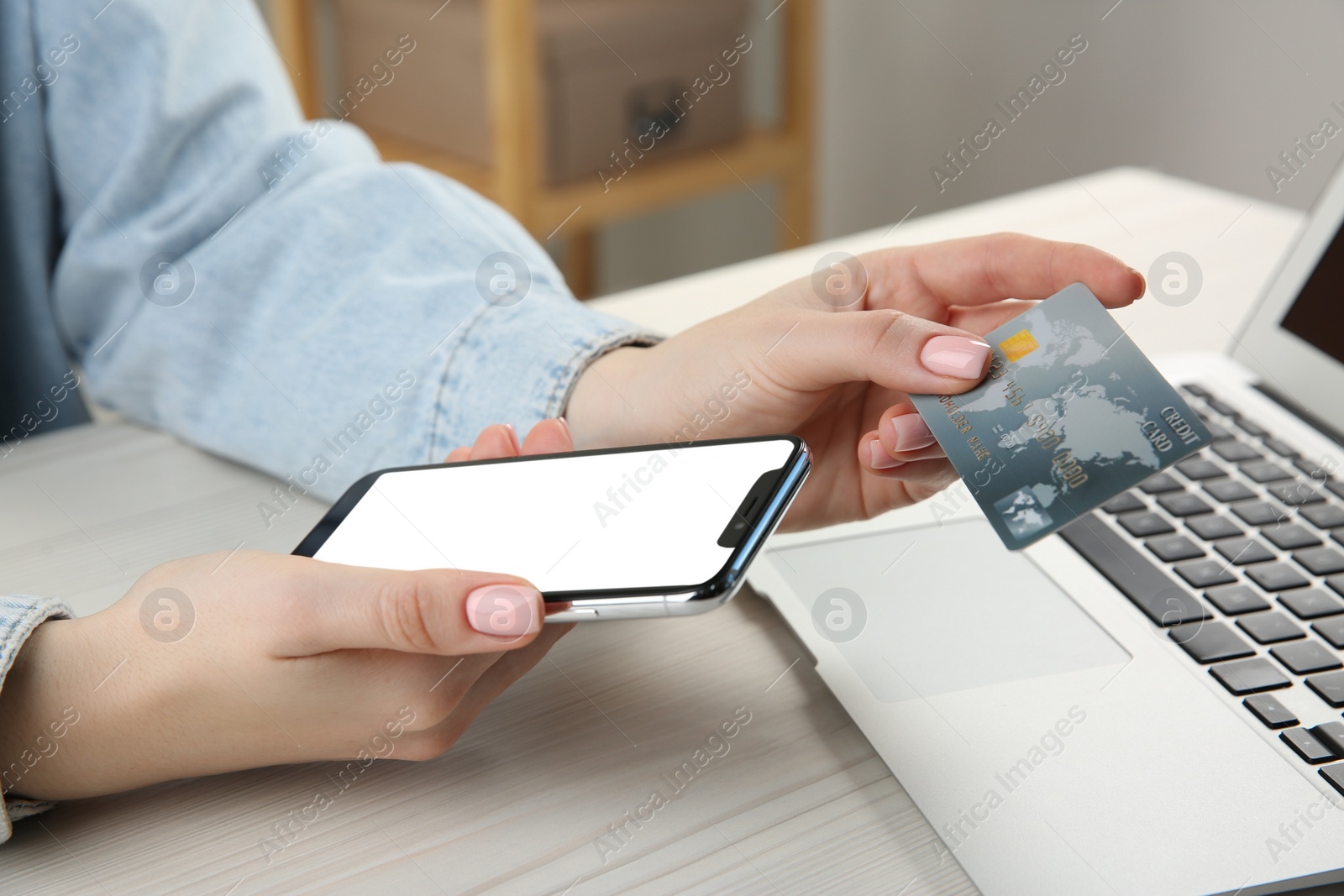 Photo of Online payment. Woman using credit card and smartphone with blank screen near laptop at white wooden table indoors, closeup