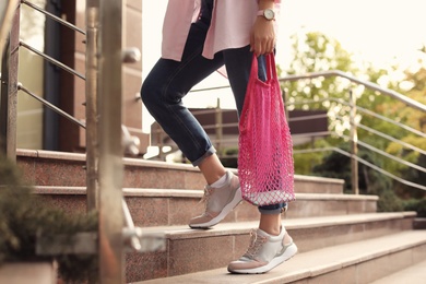 Photo of Young woman with stylish pink net bag on stairs outdoors, closeup