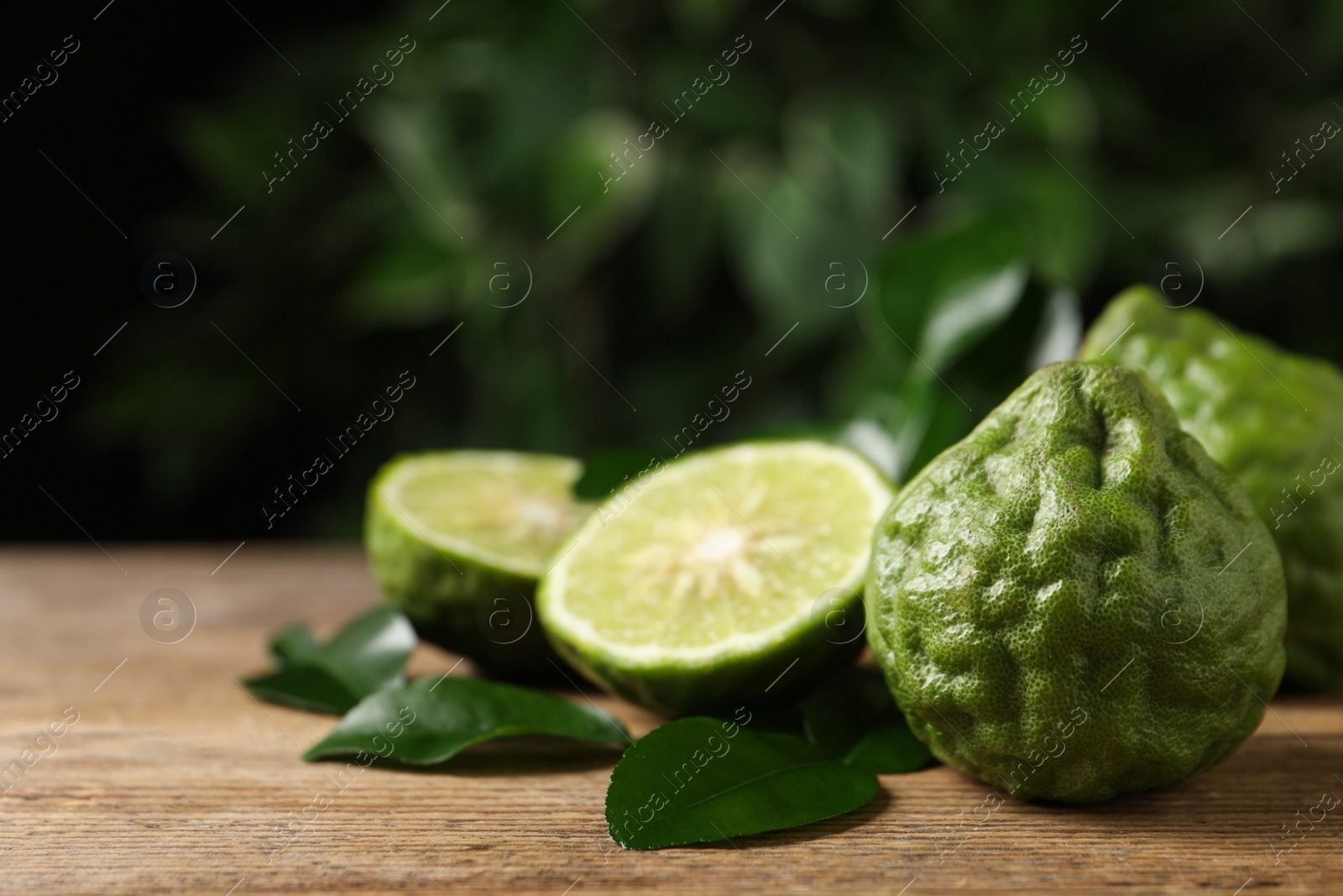 Photo of Fresh ripe bergamot fruits with green leaves on wooden table against blurred background, space for text