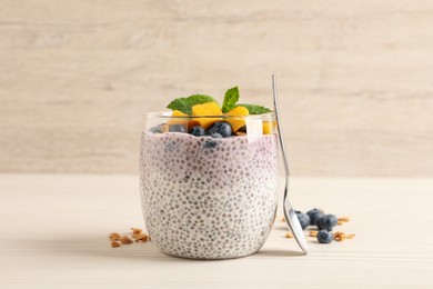 Photo of Delicious chia pudding with blueberries, mango and mint on white wooden table