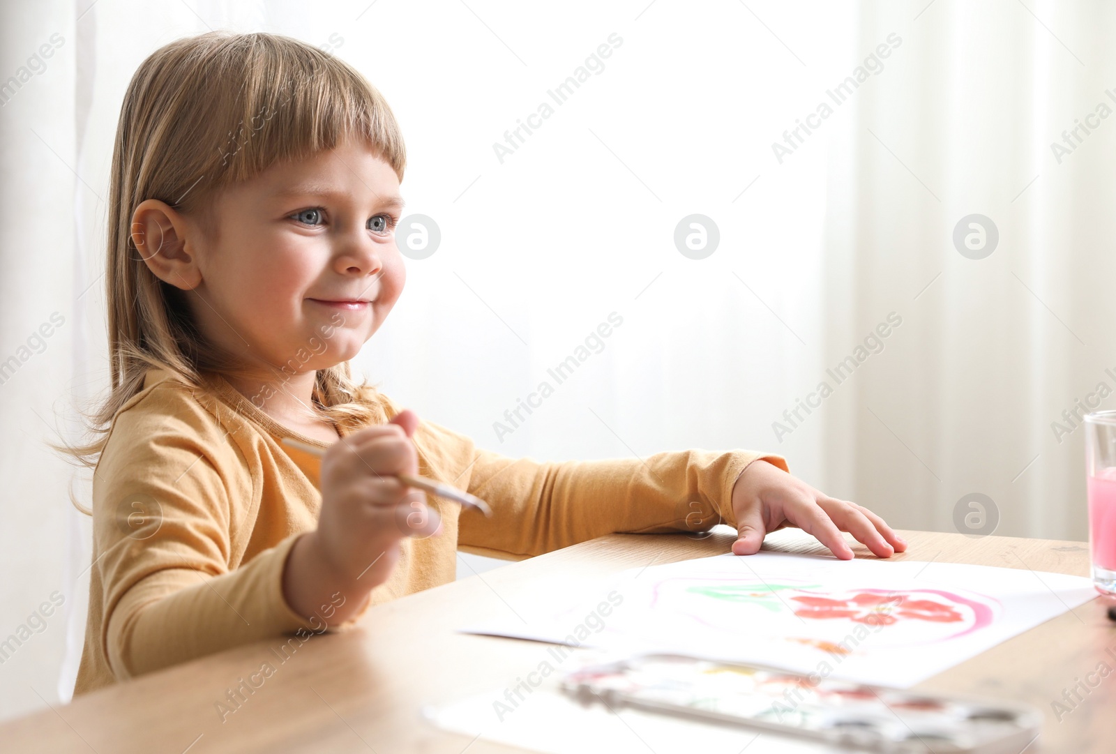 Photo of Cute little girl drawing with brush at wooden table indoors. Child`s art