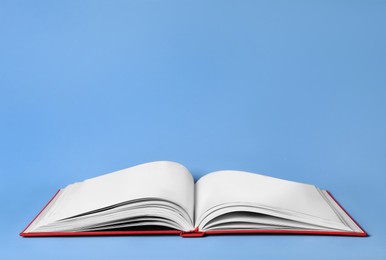 Photo of Open book with red cover on light blue background. Space for text