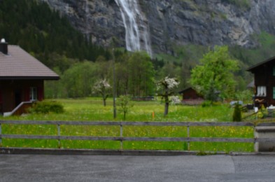 Blurred view of houses, green trees and waterfall in mountains