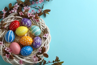 Flat lay composition with painted Easter eggs and blossoming branches on color background, space for text