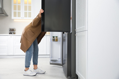Photo of Young woman looking into refrigerator in kitchen