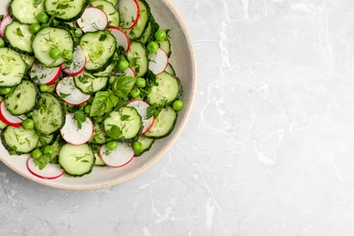 Photo of Appetizing salad with cucumbers, radish and pea in bowl on light grey table, top view. Space for text