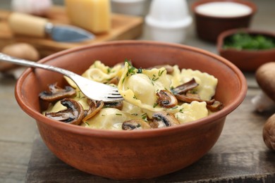 Photo of Delicious ravioli with mushrooms and fork on wooden table, closeup