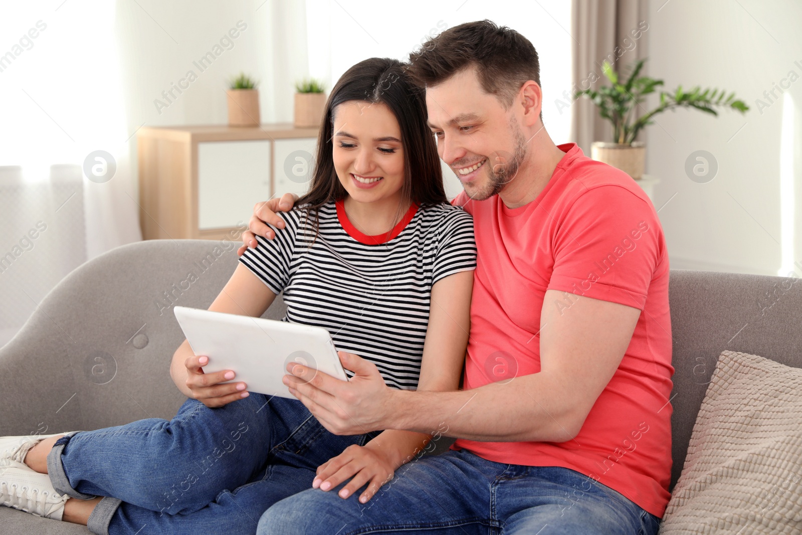 Photo of Happy couple with tablet sitting on couch at home