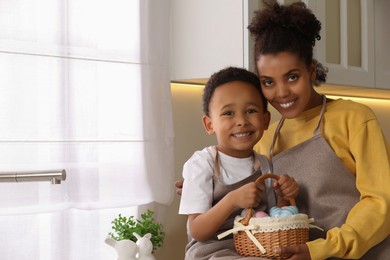 Happy African American mother and her cute son with Easter eggs in kitchen