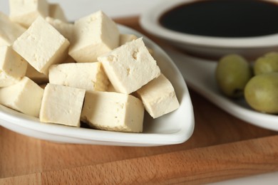 Pieces of delicious tofu and olives on wooden board, closeup. Soybean curd