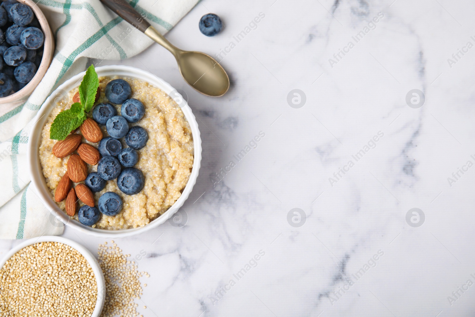 Photo of Bowl of delicious cooked quinoa with almonds and blueberries on white marble table, flat lay. Space for text