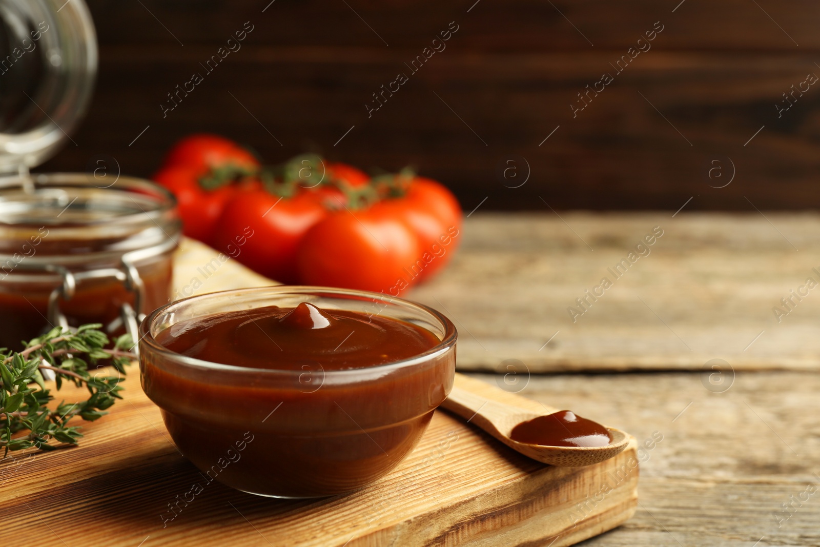 Photo of Tasty barbeque sauce in bowl and spoon on wooden table, closeup. Space for text