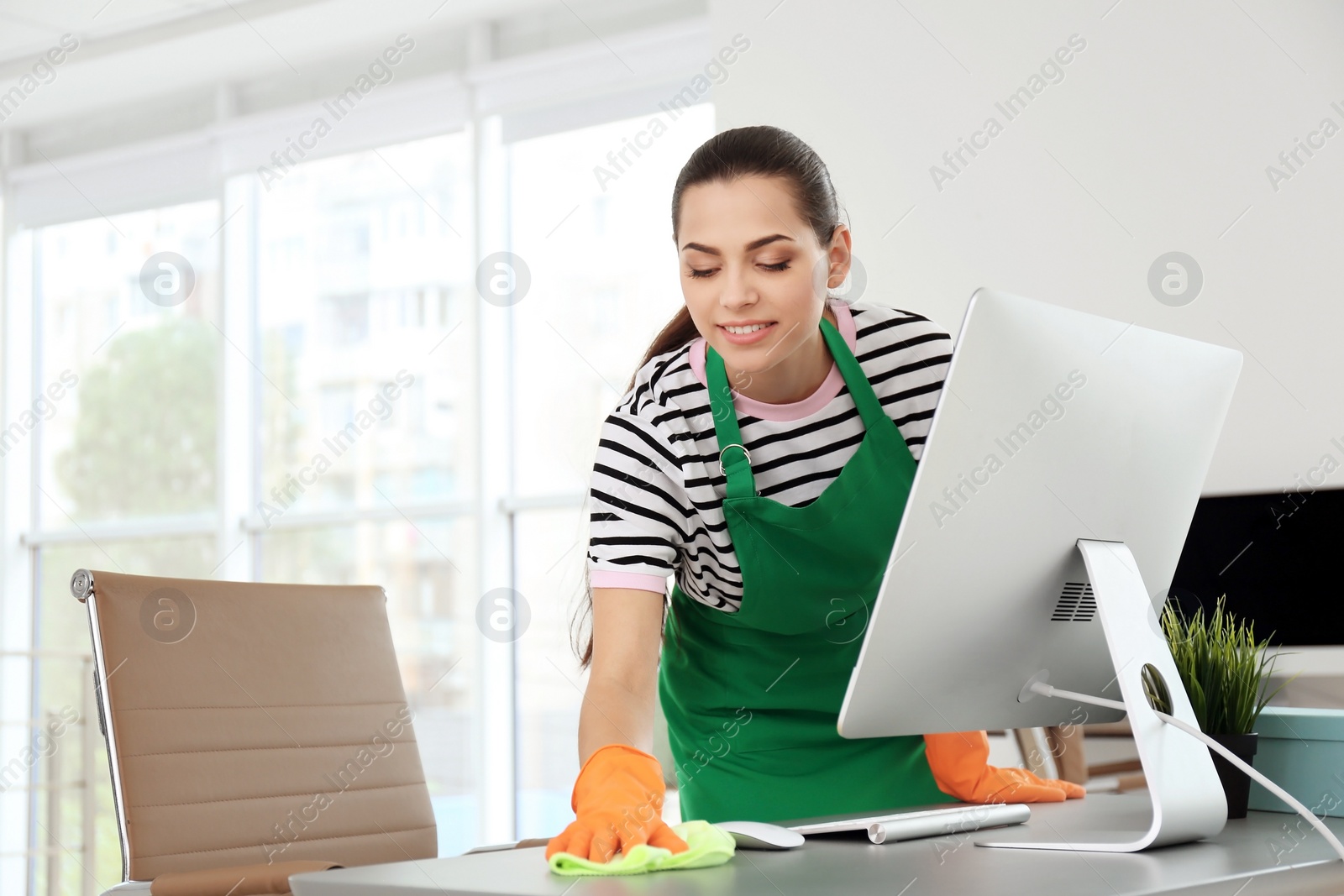 Photo of Young woman in apron and gloves cleaning office