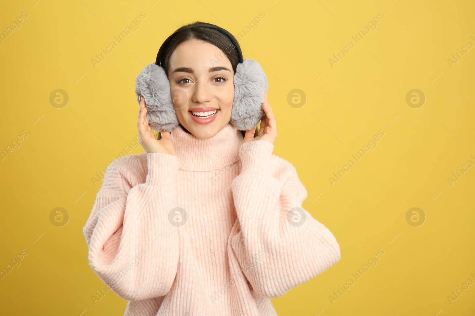 Photo of Beautiful young woman wearing earmuffs on yellow background