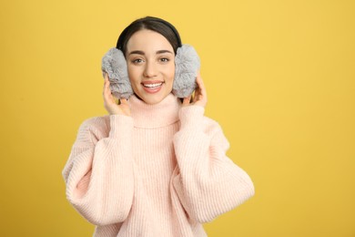 Beautiful young woman wearing earmuffs on yellow background