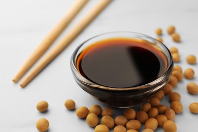 Soy sauce in bowl and soybeans on white table, closeup