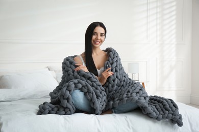 Young woman with chunky knit blanket on bed at home