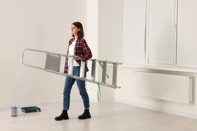 Photo of Young beautiful woman with metal stepladder indoors. Room renovation