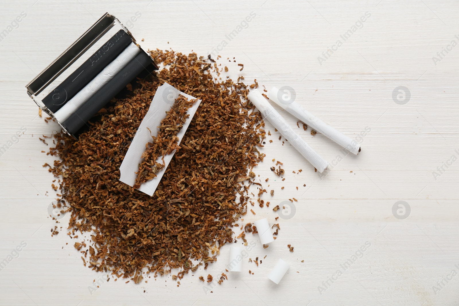 Photo of Flat lay composition with roller and tobacco on white wooden table, space for text. Making hand rolled cigarettes
