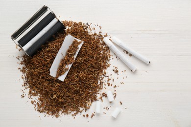 Flat lay composition with roller and tobacco on white wooden table, space for text. Making hand rolled cigarettes