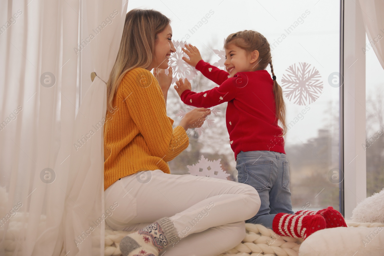 Photo of Happy mother and daughter decorating window with paper snowflakes indoors