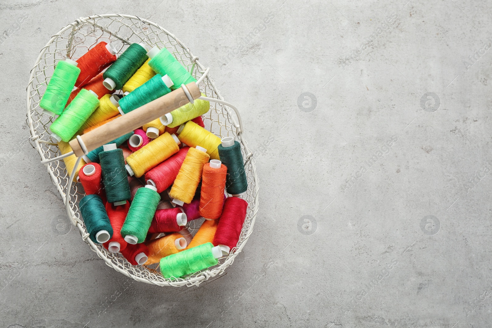 Photo of Metal basket with color sewing threads on grey background, top view