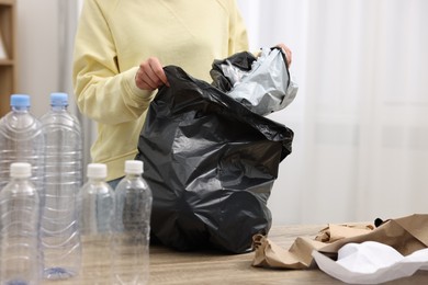 Photo of Woman with plastic bag separating garbage at table in room, closeup
