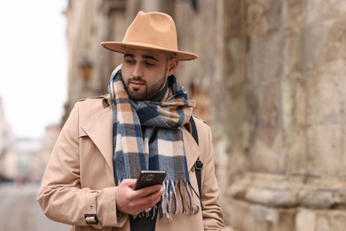 Photo of Handsome man in warm scarf with smartphone outdoors. Space for text