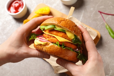 Photo of Woman holding tasty vegetarian burger over table, top view