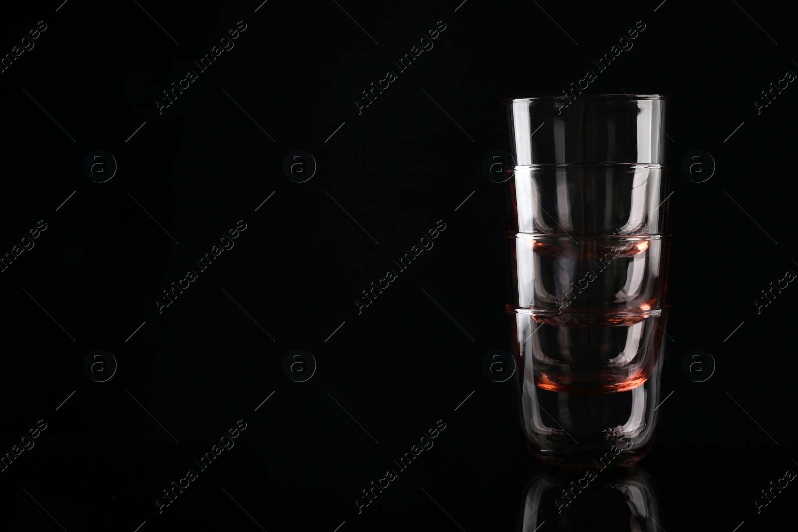 Photo of Stack of empty colorful whiskey glasses on black background, space for text