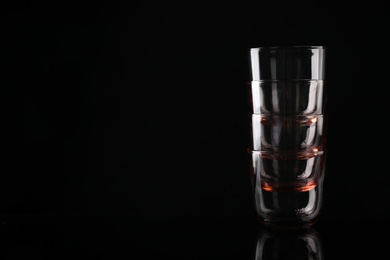 Photo of Stack of empty colorful whiskey glasses on black background, space for text