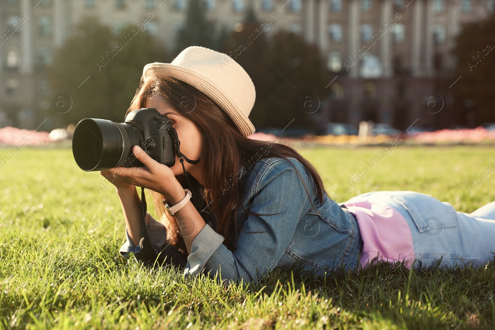 Photo of Young female photographer taking photo with professional camera on grass outdoors