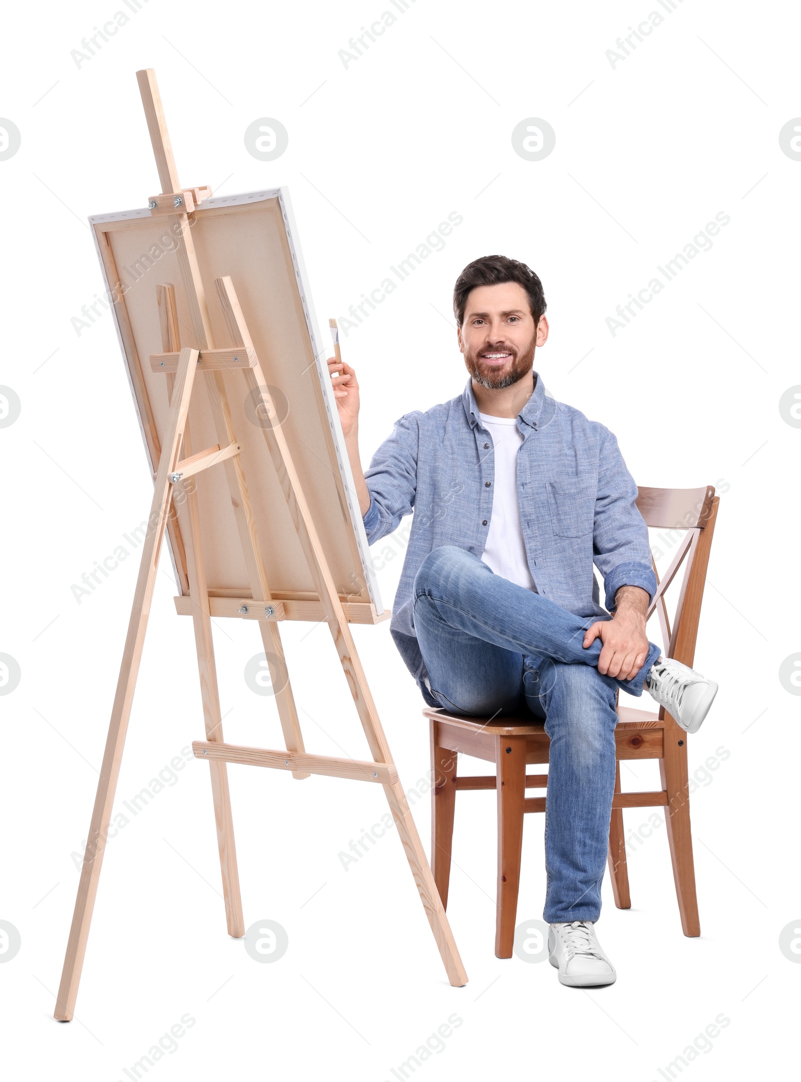 Photo of Happy man painting with brush against white background. Using easel to hold canvas