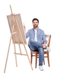 Photo of Happy man painting with brush against white background. Using easel to hold canvas