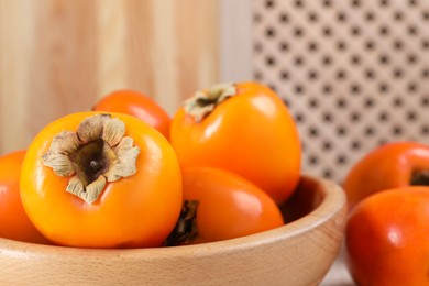 Photo of Delicious ripe persimmons in bowl on blurred background, closeup