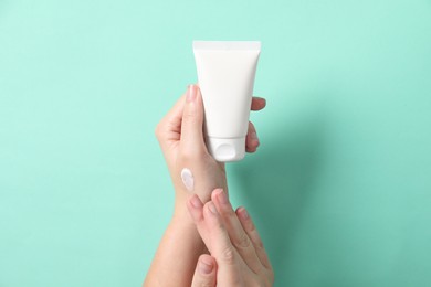 Photo of Woman with tube applying cosmetic cream onto her hand on turquoise background, closeup