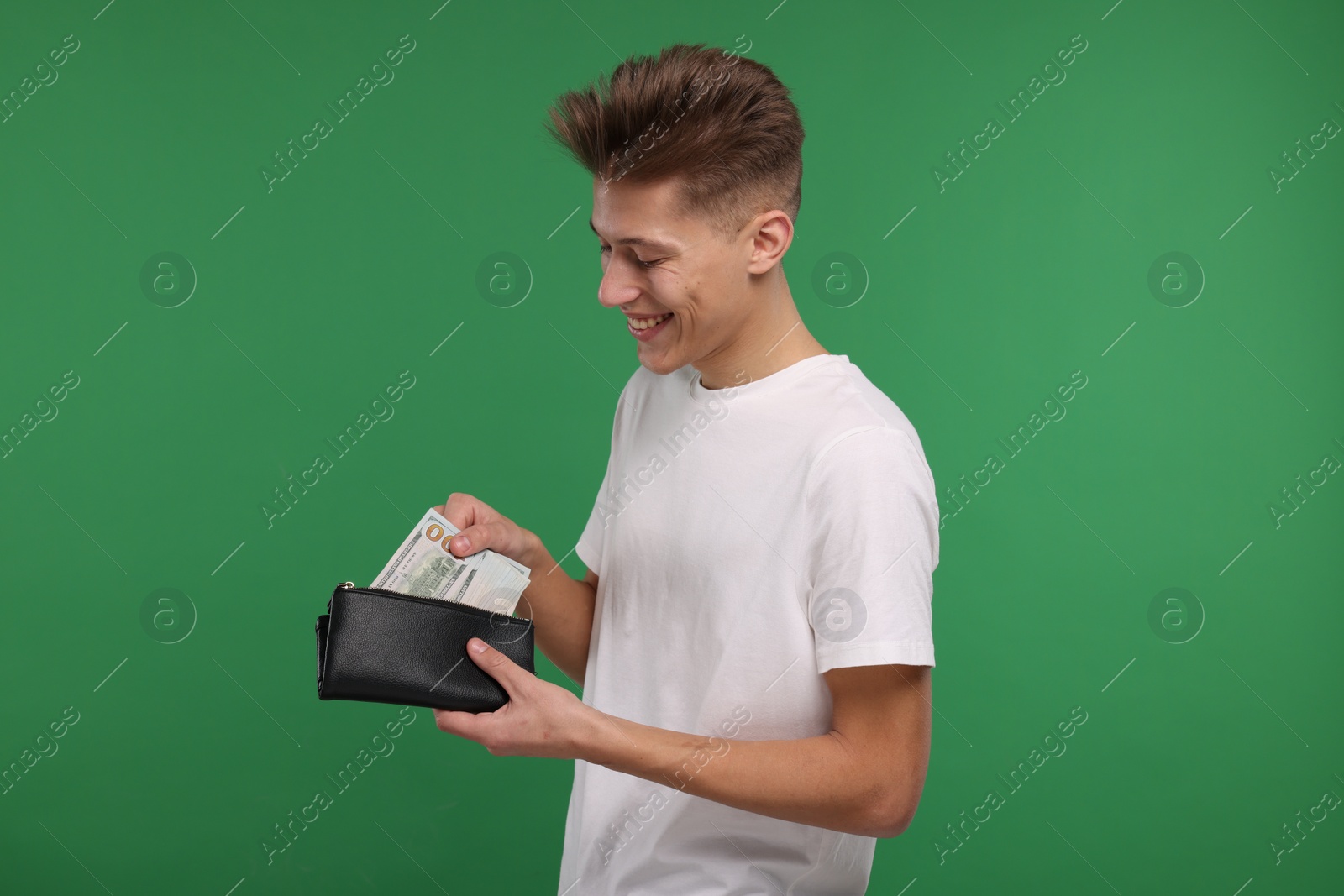 Photo of Happy man putting money into his wallet on green background