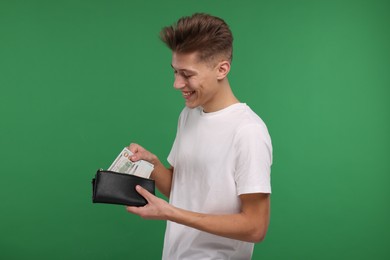 Photo of Happy man putting money into his wallet on green background