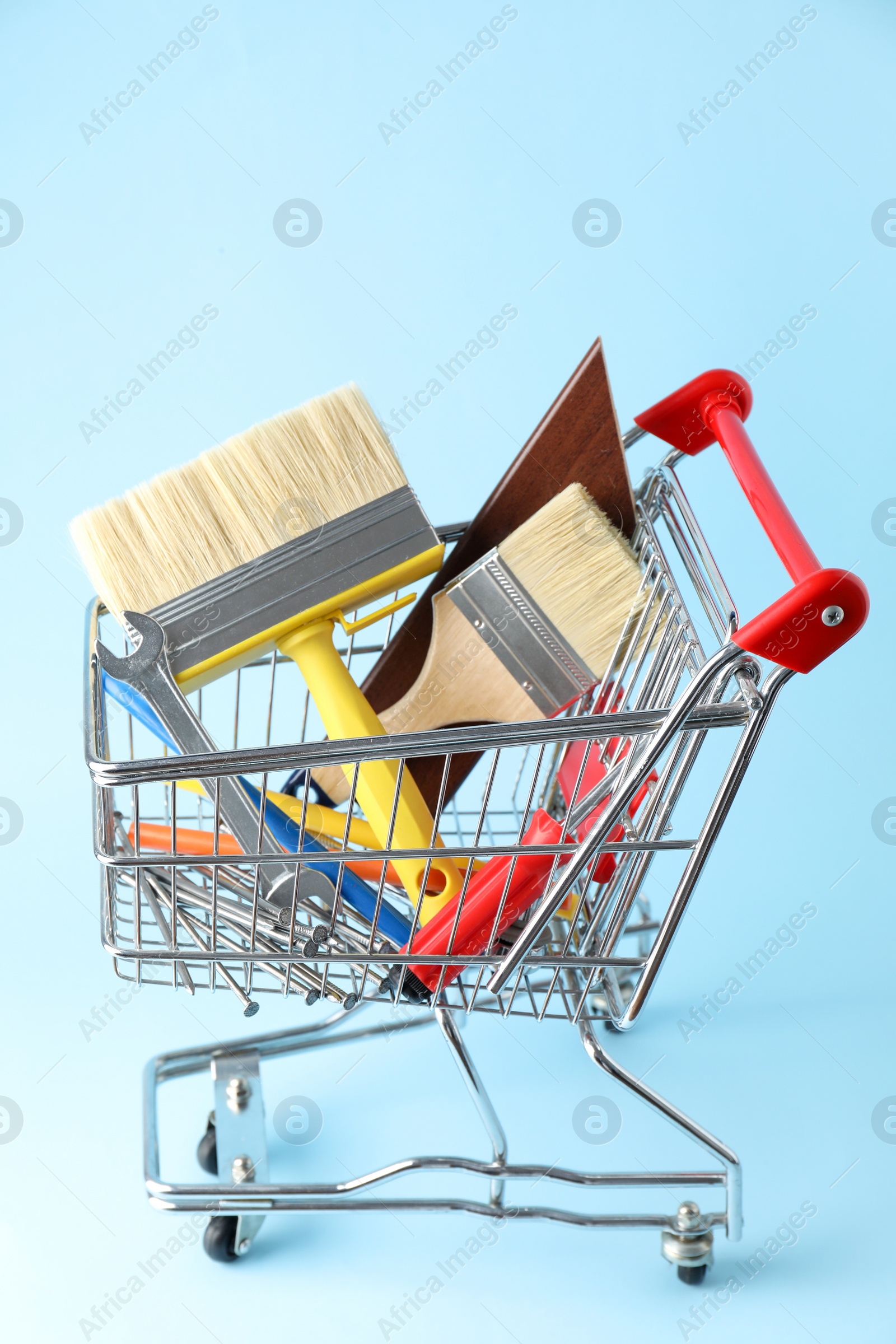 Photo of Different construction tools in shopping cart on light blue background