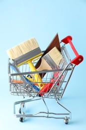 Photo of Different construction tools in shopping cart on light blue background