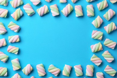 Photo of Frame of delicious colorful marshmallows on light blue background, flat lay. Space for text