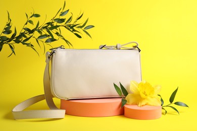 Photo of Stylish presentation of bag, green leaves and daffodil flower on yellow background