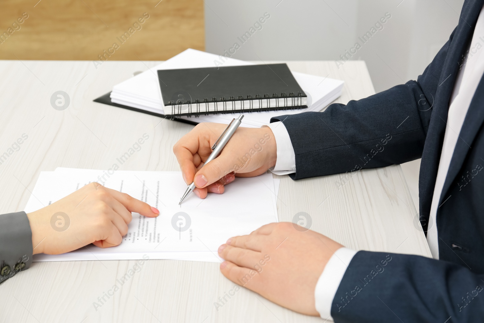 Photo of Woman pointing at document and man putting signature at wooden table, closeup