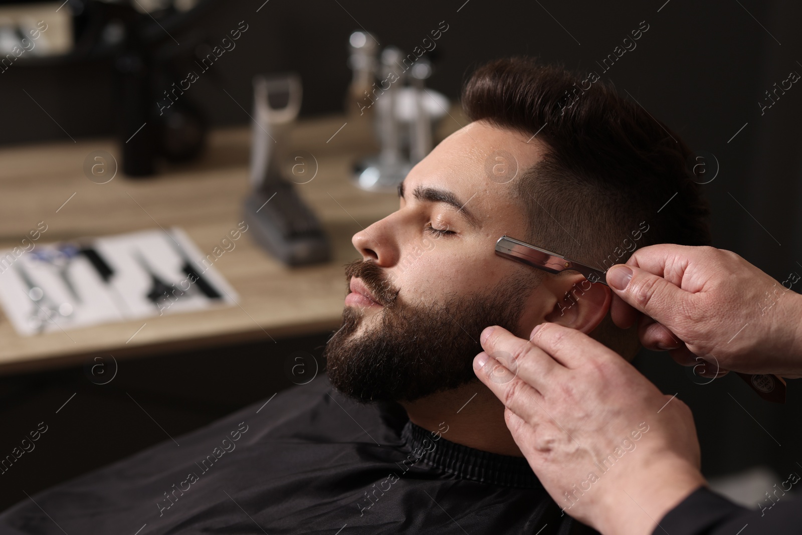 Photo of Professional barber shaving client's beard with blade in barbershop, closeup